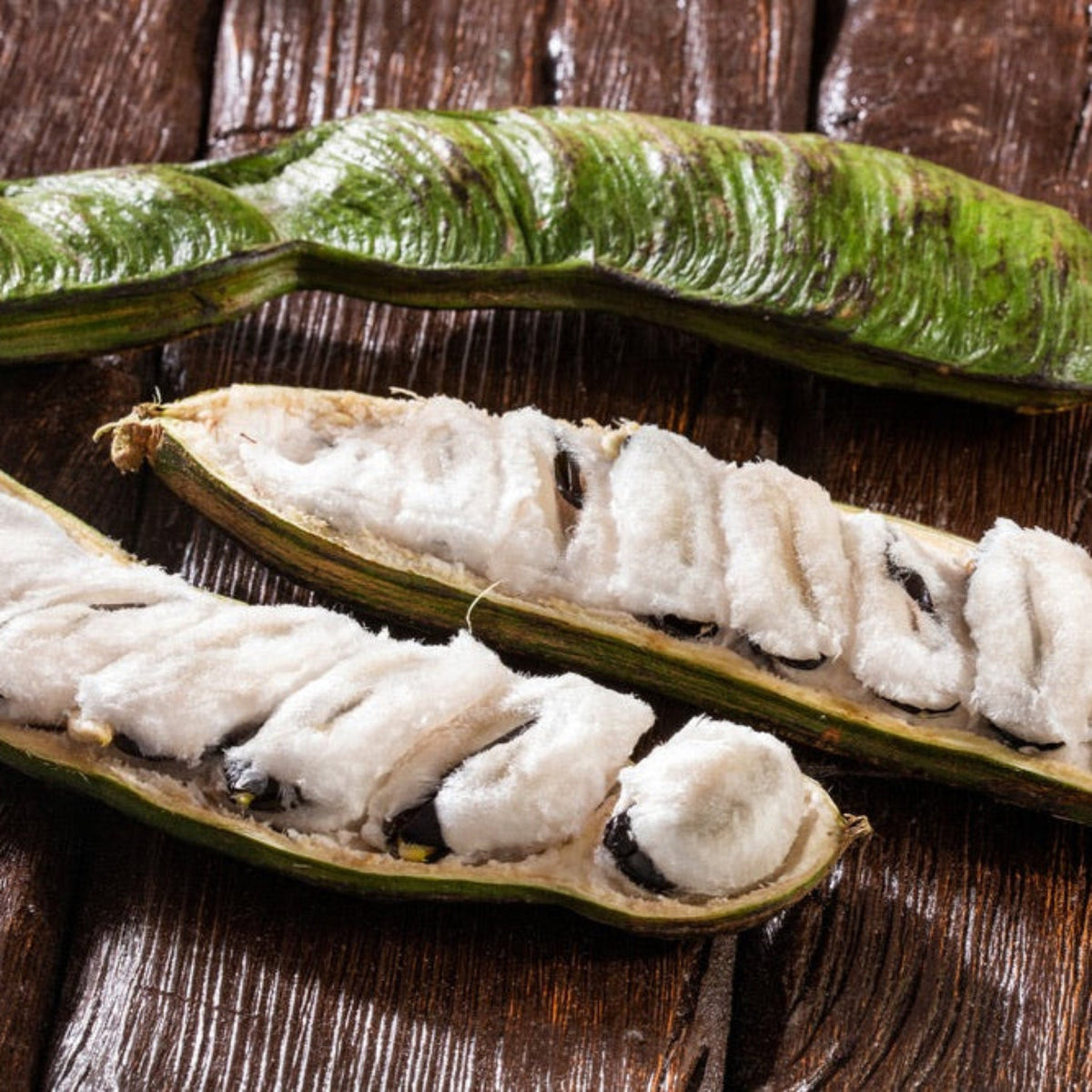 Open Ice Cream Bean fruit revealing white fibers inside on a wooden surface