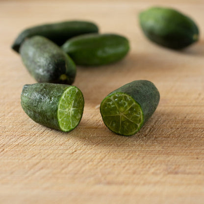 Australian Finger Lime fruit, one cut in half, on a wooden surface