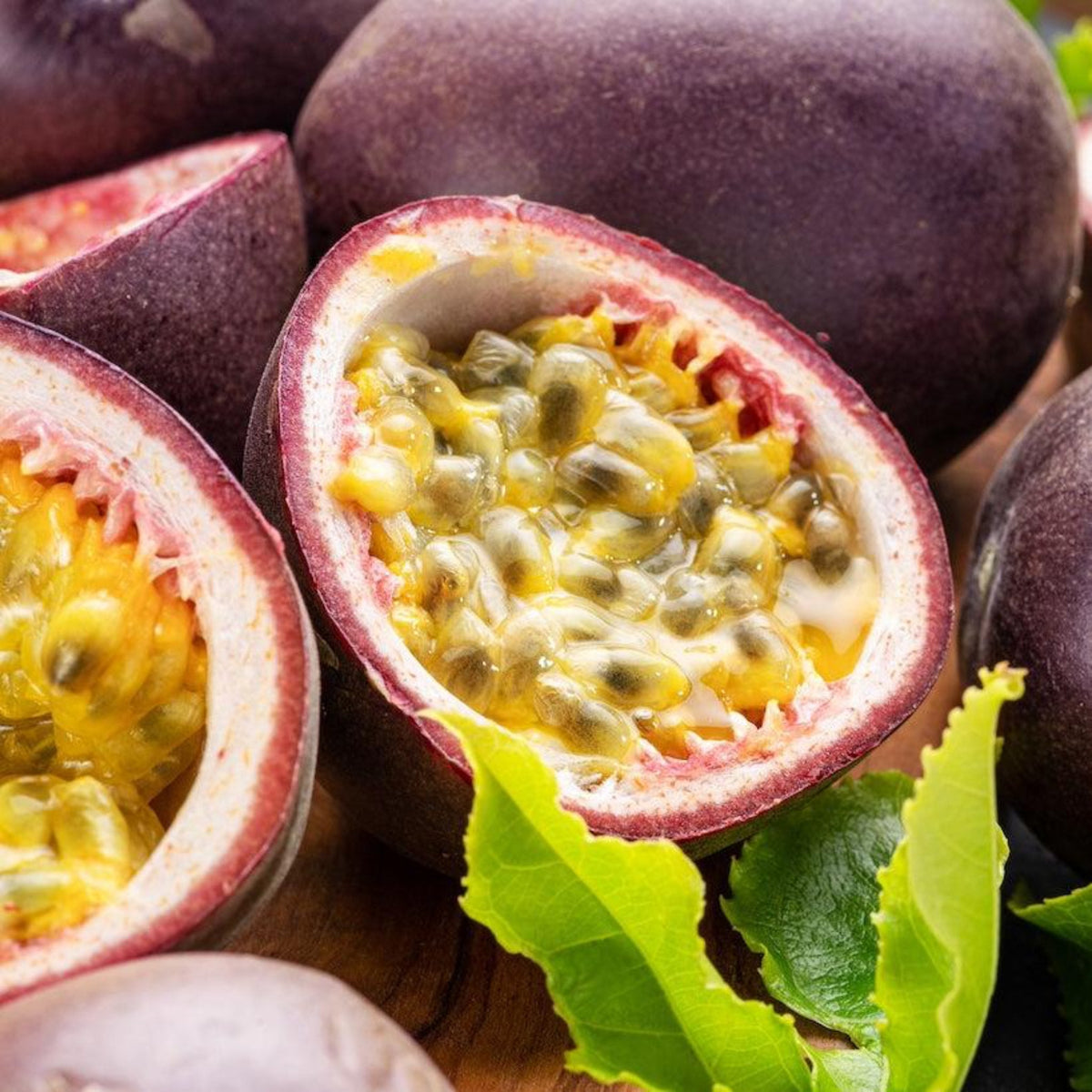 Halved passion fruit revealing juicy yellow pulp and seeds next to whole purple fruits.