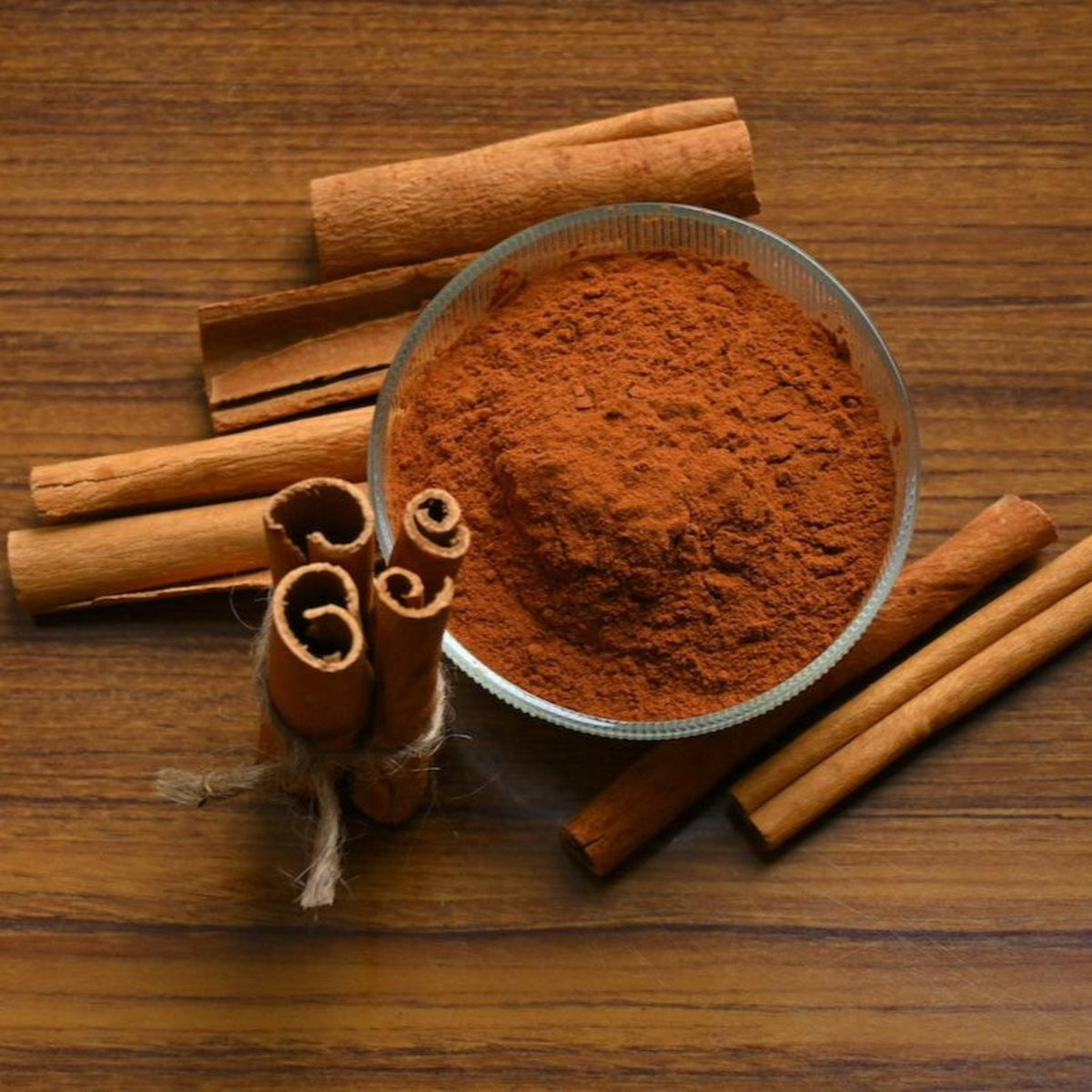 Bowl of ground cinnamon powder surrounded by whole cinnamon sticks on a wooden surface.