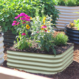 The 15-inch tall small corrugated metal raised garden bed in a mist green color, filled with various colorful flowers including pink, yellow, and purple, set in a garden bed with mulch and other plants.