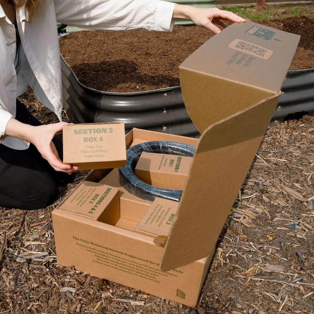 Person opening a cardboard box with gardening epic irrigation components in an outdoor setting.