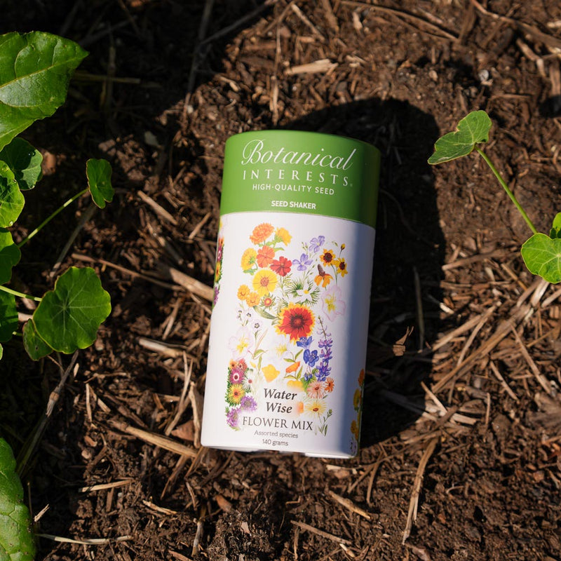 Botanical Interests Water Wise Flower Mix Seed Shaker canister on soil with plants around
