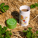 Opened Water Wise Flower Mix Seed Shaker canister on a straw background with plants around