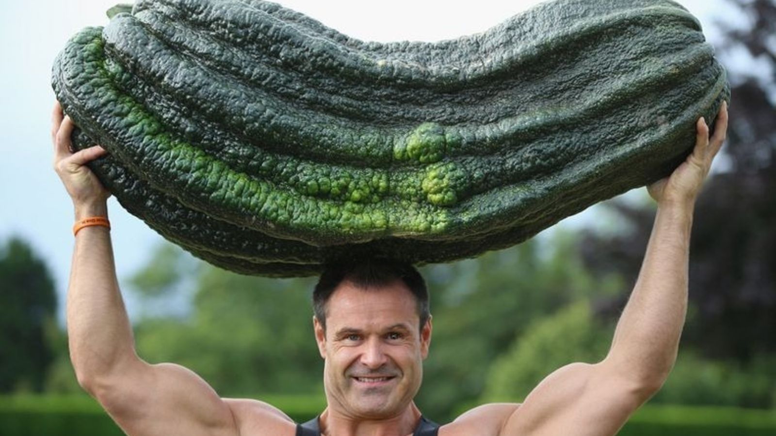 Jonathan Walker lifts a marrow over his head, holding it with bare hands with trees blurred in the background