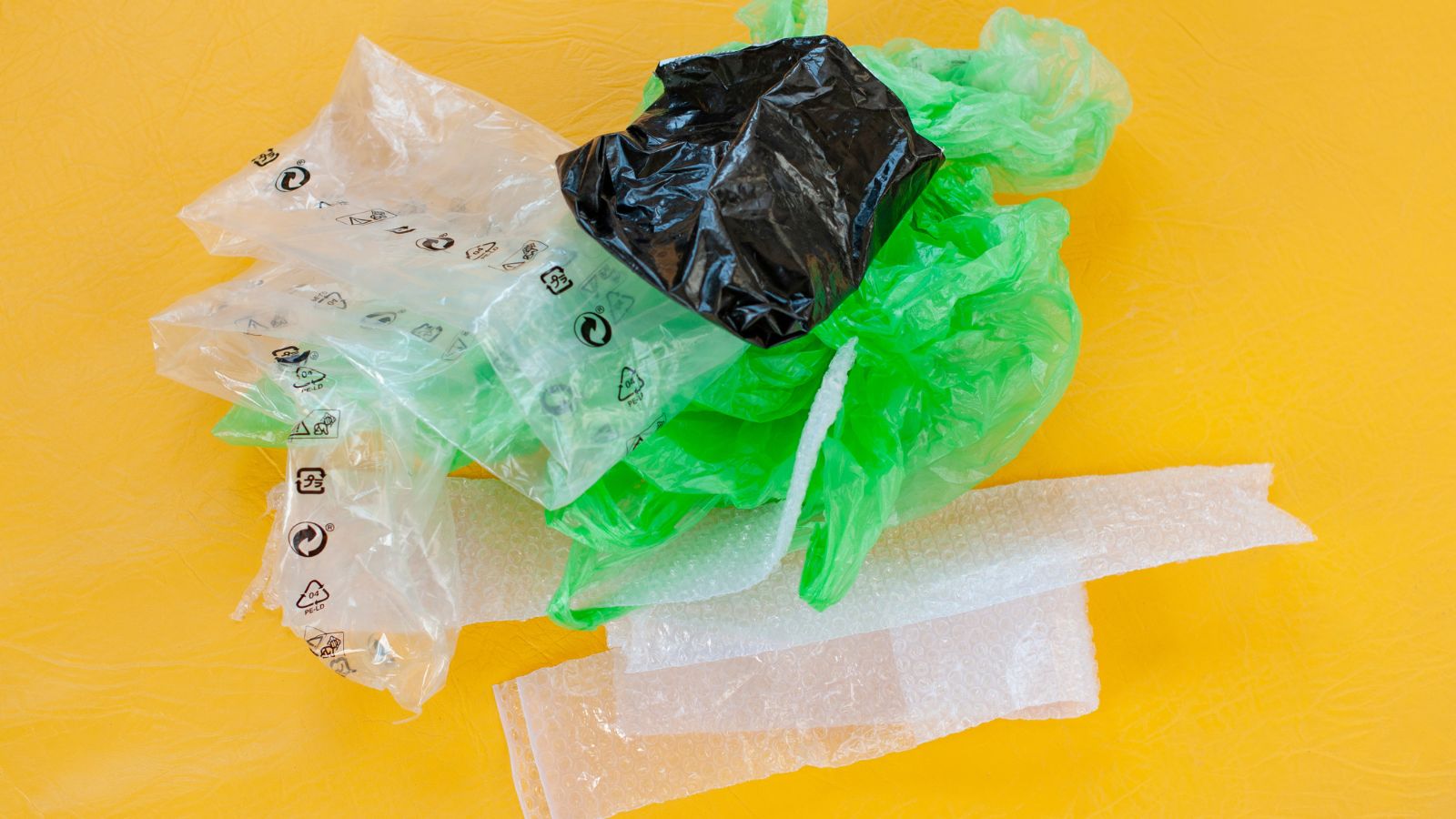 An overhead shot of a small pile of various LDPE bags on a yellow surface, in a well lit area indoors