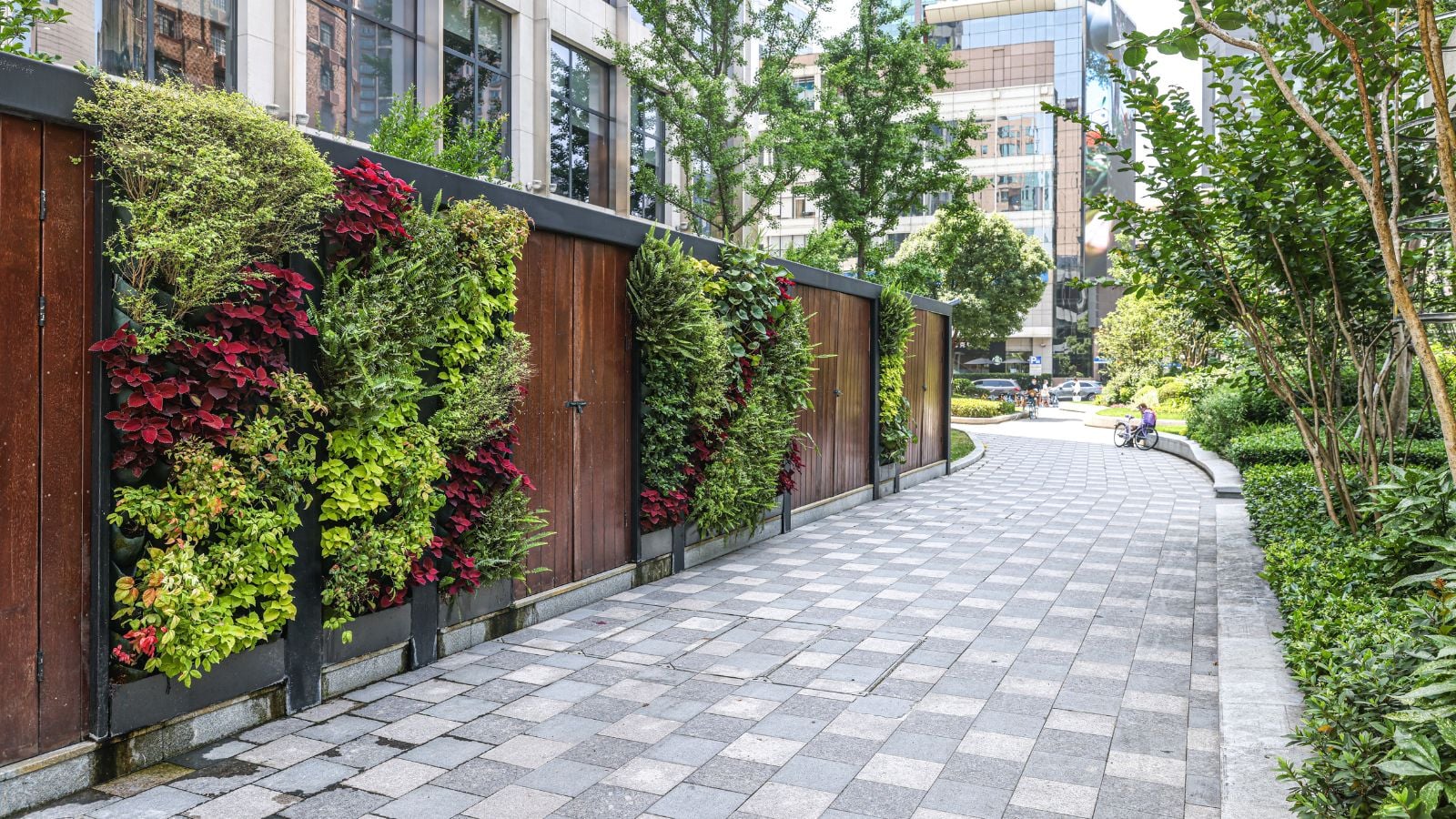 An outdoor wall with a Banded Vertical Striped Garden appearing to have different plants along a concrete walkway