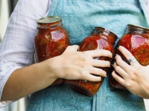 A person holding jars of salsa using crops of a salsa garden while the person wore a blue apron
