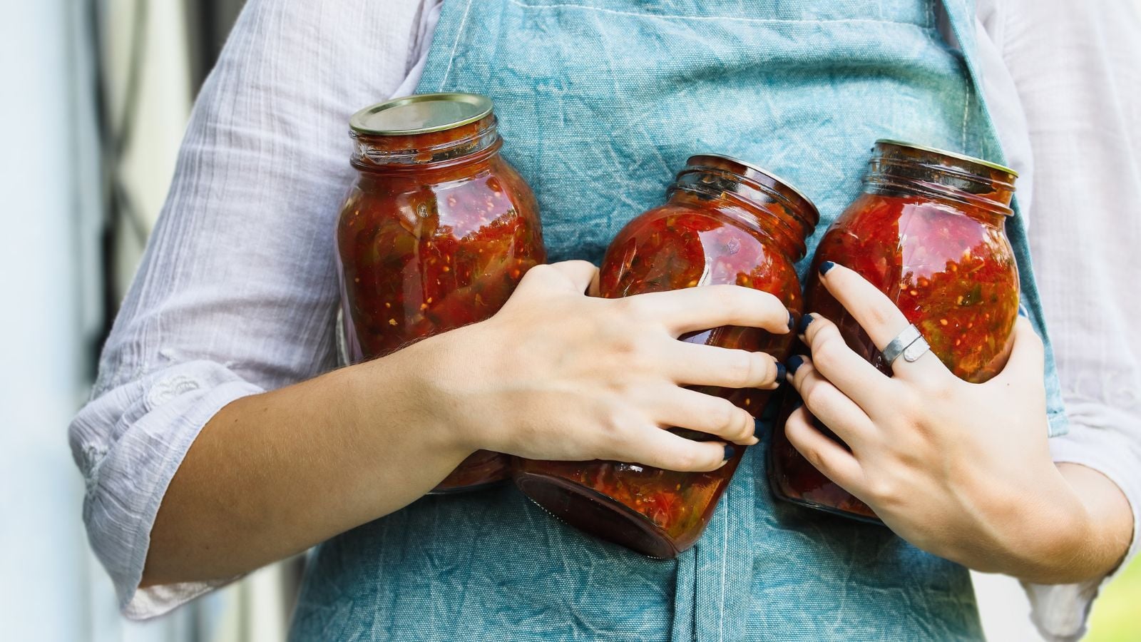 A person holding jars of salsa using crops of a salsa garden while the person wore a blue apron