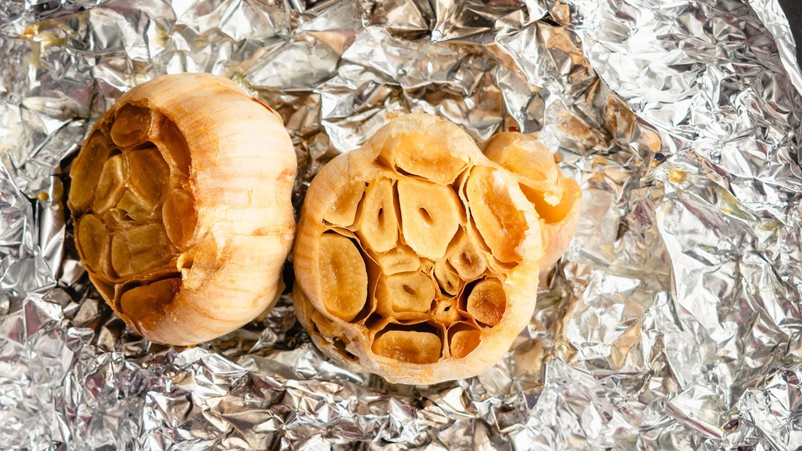 Roasted Allium sativum appearing to have a brown color, placed in a crumpled aluminum foil