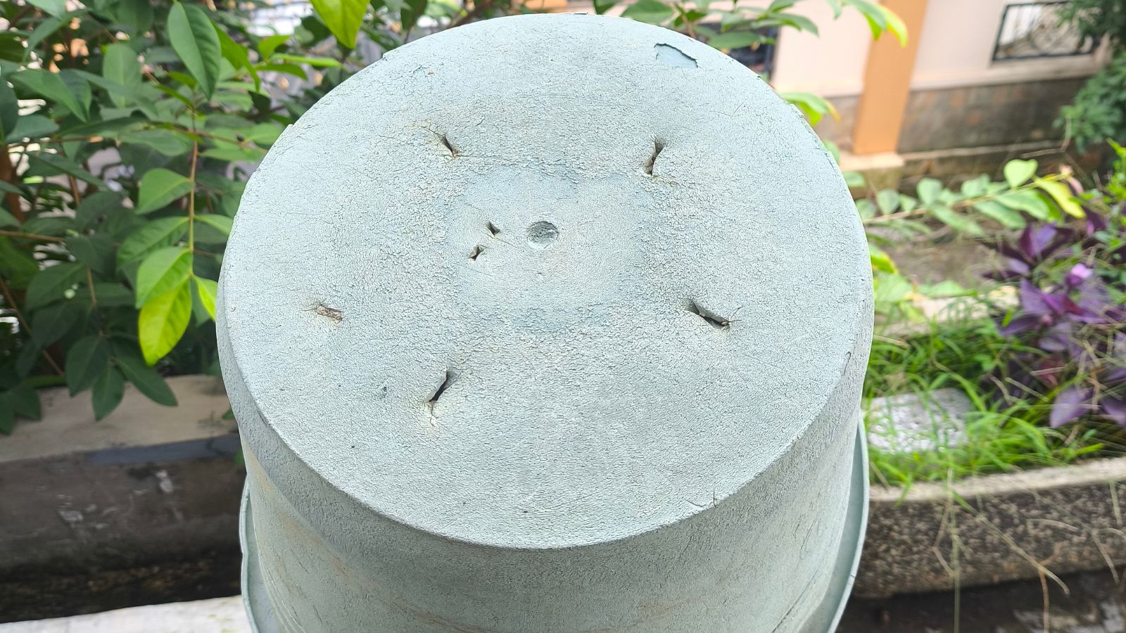 A close-up and overhead shot of a bottom of a bucket with slits as drainage holes