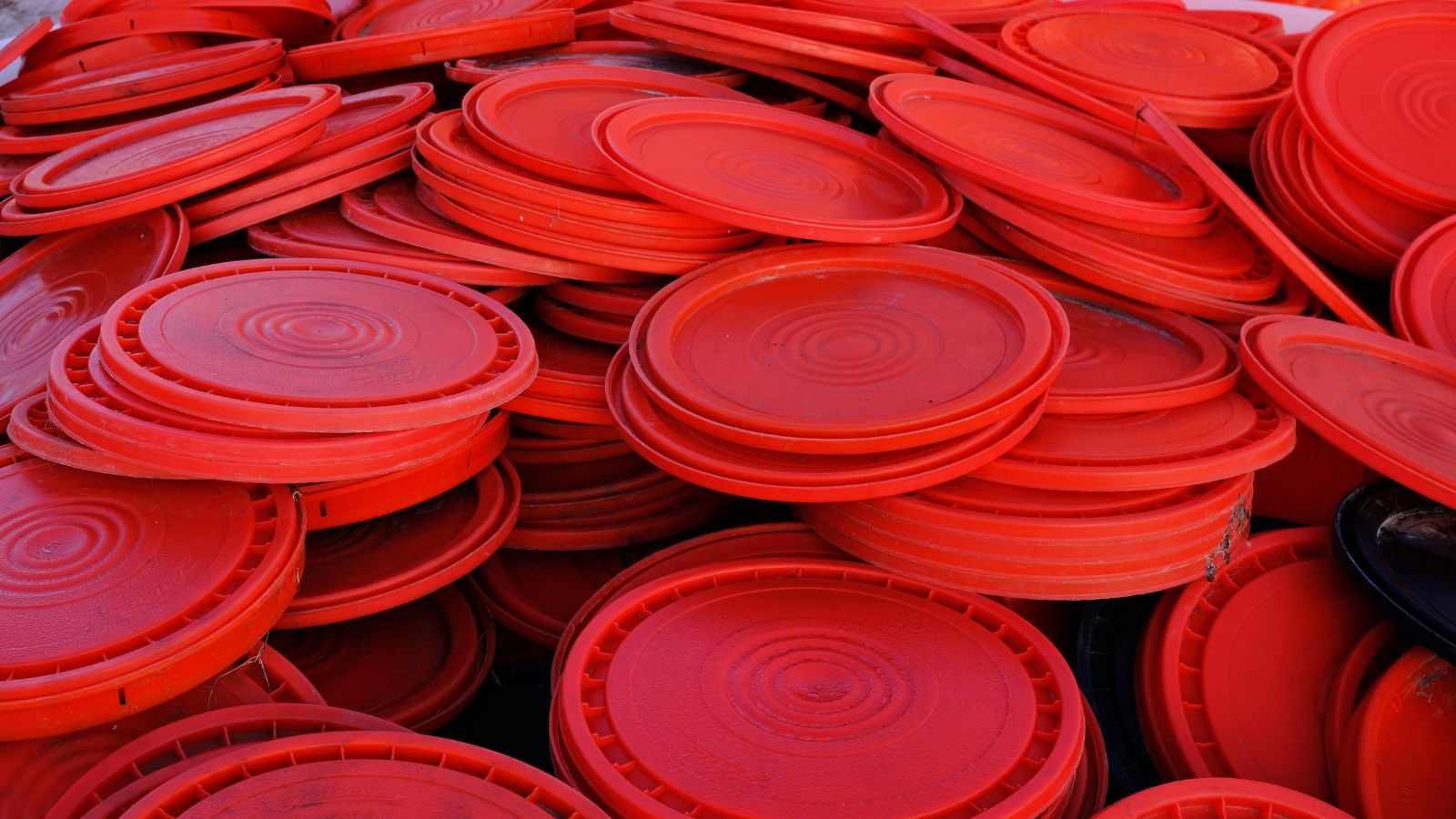 A close-up shot of a large pile or red-orange colored bucket lids, all placed in a well lit area
