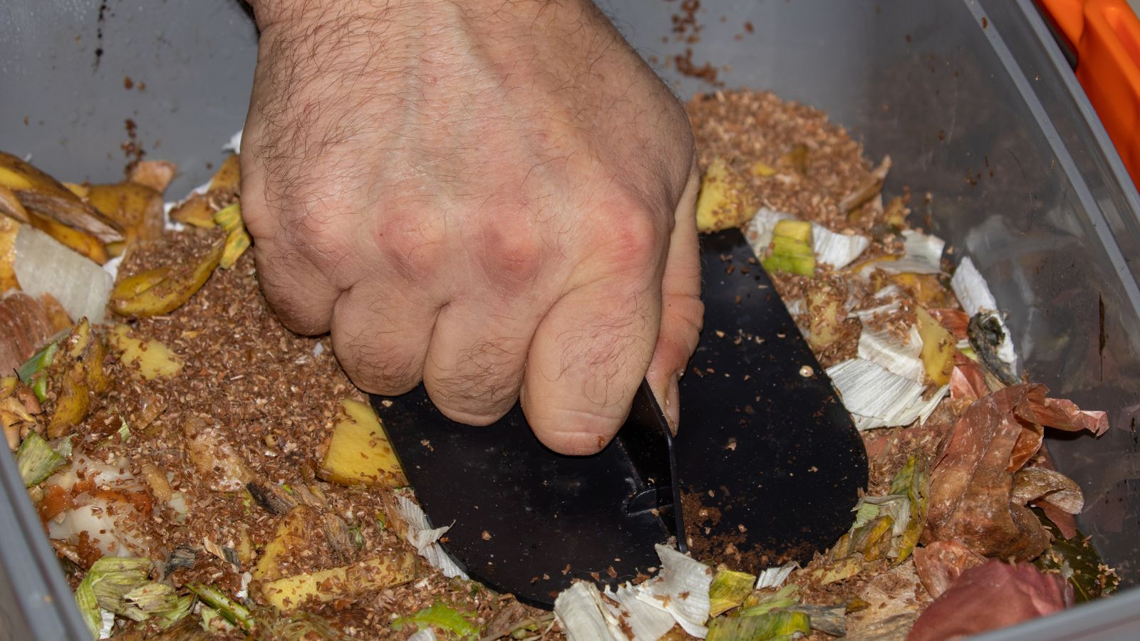 A close-up shot of a person in the process of tightly packing compost in a bucket