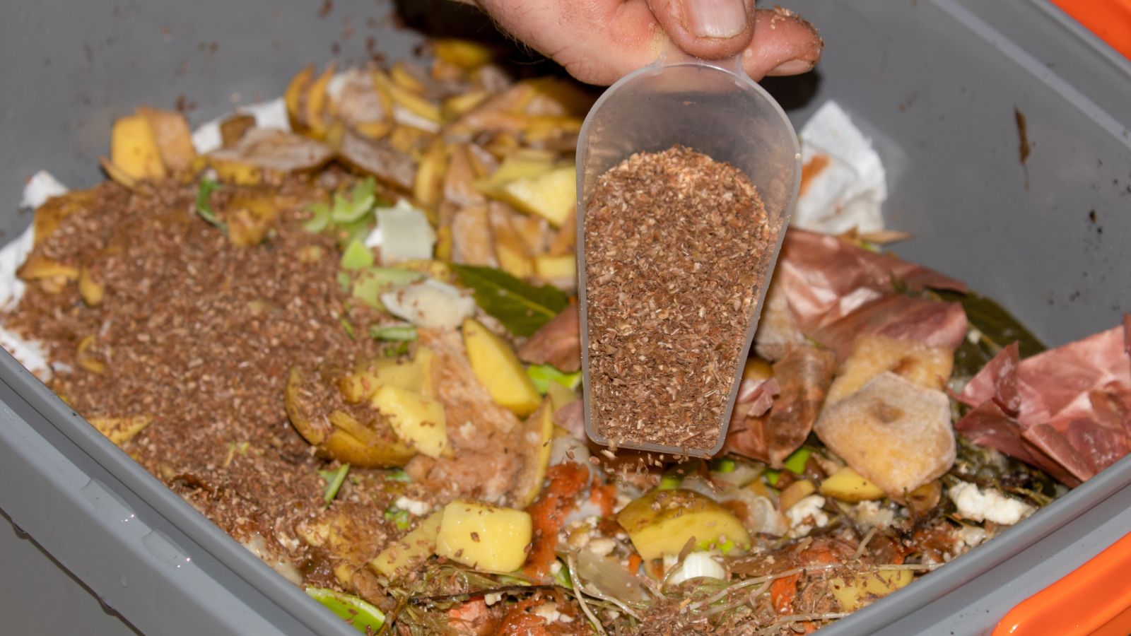 A close-up shot of a person's hand holding a scooper filled with bran-like material in a well lit area indoors