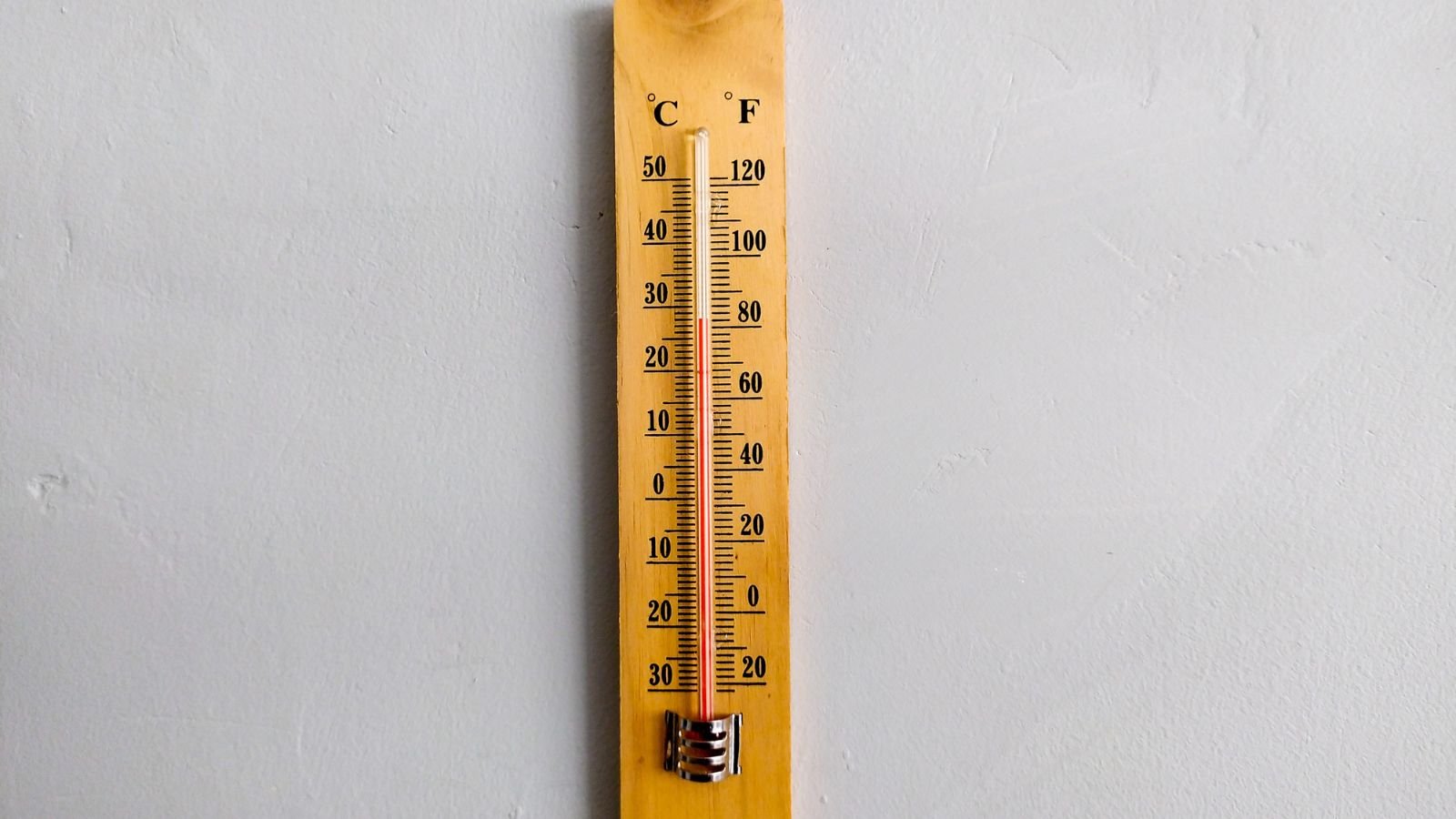 A wooden thermometer on a gray wall appearing to have a red line in the middle inside a glass tube held by a metal fitting