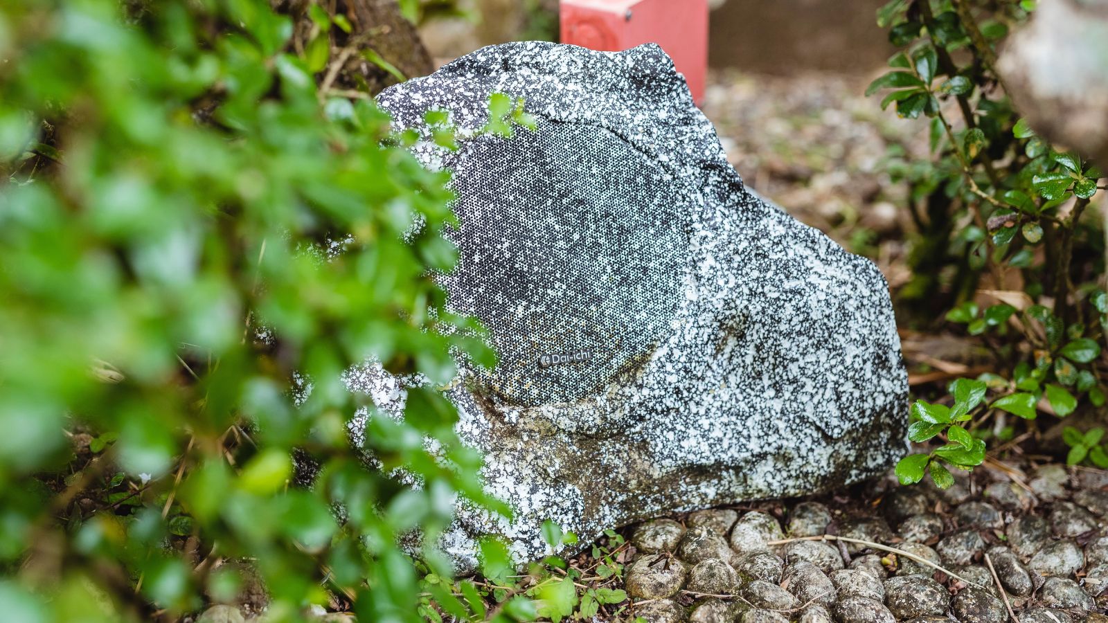 Outdoor speaker shaped like a rock appearing weatherproof and strong placed among different plants