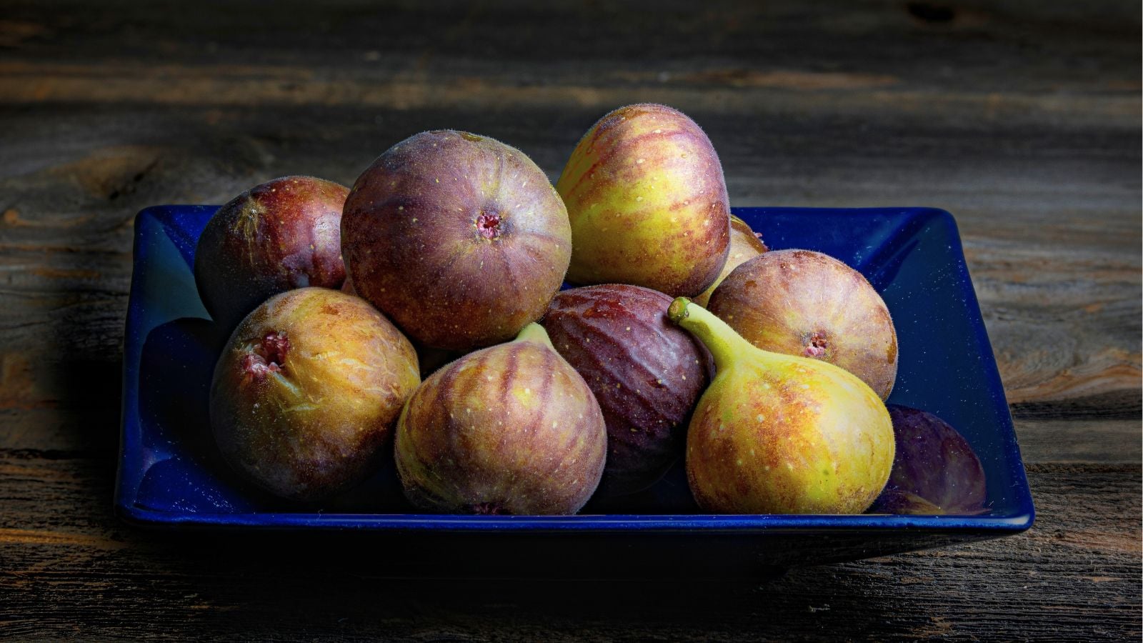 A close-up shot of a plate filled with a small pile of freshly harvested fruits. all placed on a wooden surface indoors