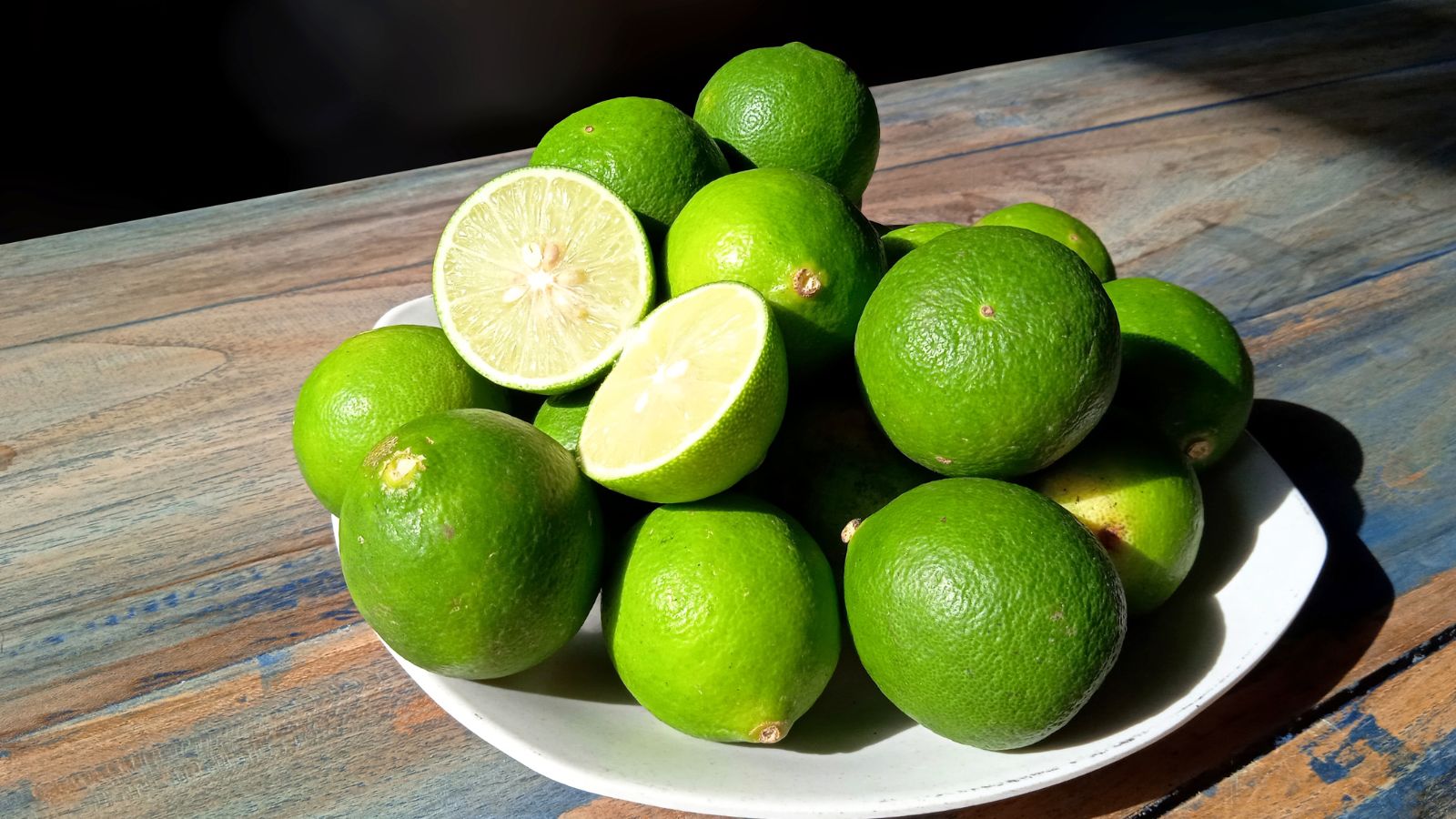 Citrus aurantifolia fruits on a plate, placed on a wooden table with lots of bright, warm sunlight
