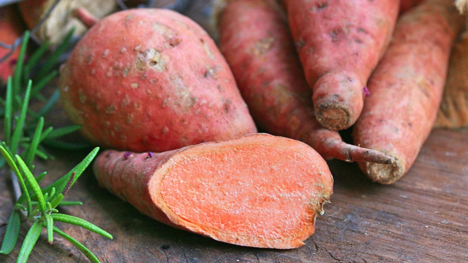 A close-up shot of a small pile of red colored crops with orange flesh called Garnet, all piled on top of each other on a wooden surface