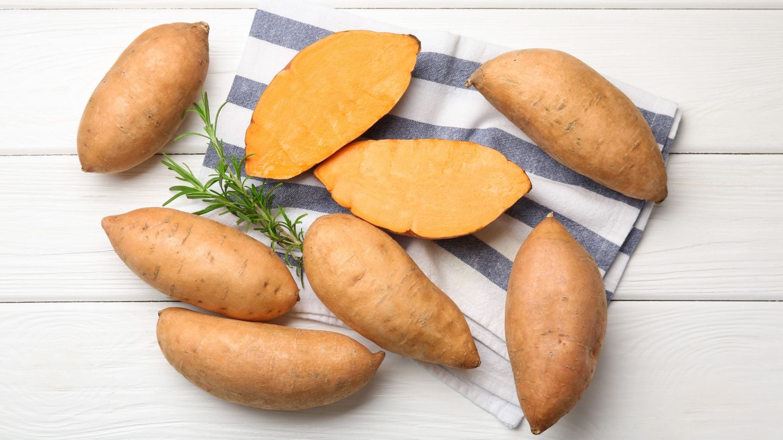 An overhead and close-up shot of a small composition of copper colored crops, with a light orange flesh called the Porto Rico, all placed on top of a wooden surface indoors