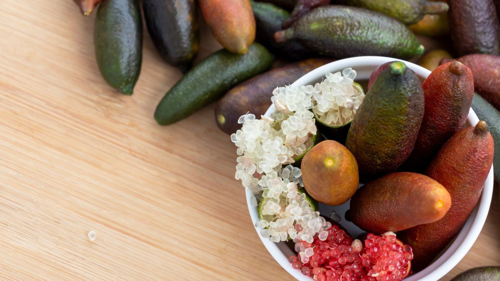 Citrus australasica pieces placed on a wooden surface, having multiple pieces placed in a small white cup, revealing some pieces split open