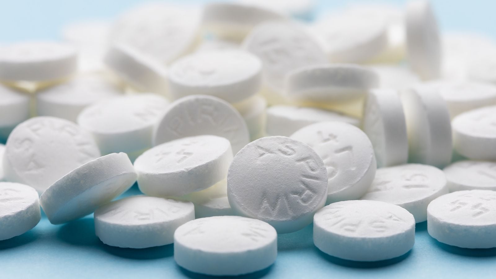 A pile of white Aspirin tablets, randomply placed on top of one another on a light blue surface