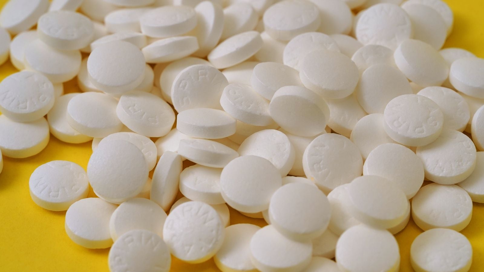 A pile of white tables with each piece randomly dumped on a yellow surface, under mild light