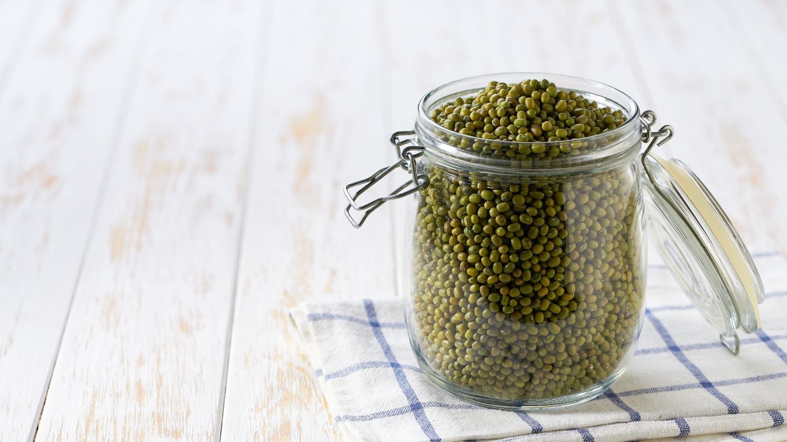 A close-up shot of a jar filled to the brim with harvested legumes, placed on top of a wooden surface indoors