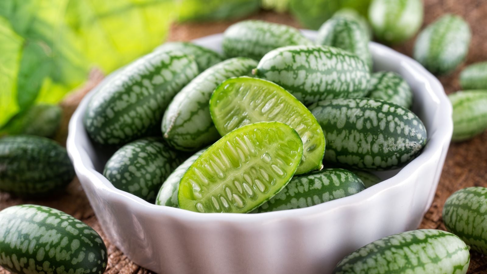 A bowl of Melothria scabra crops, placed in a small and white bowl on a brown wooden surface with some pieces scattered on the table