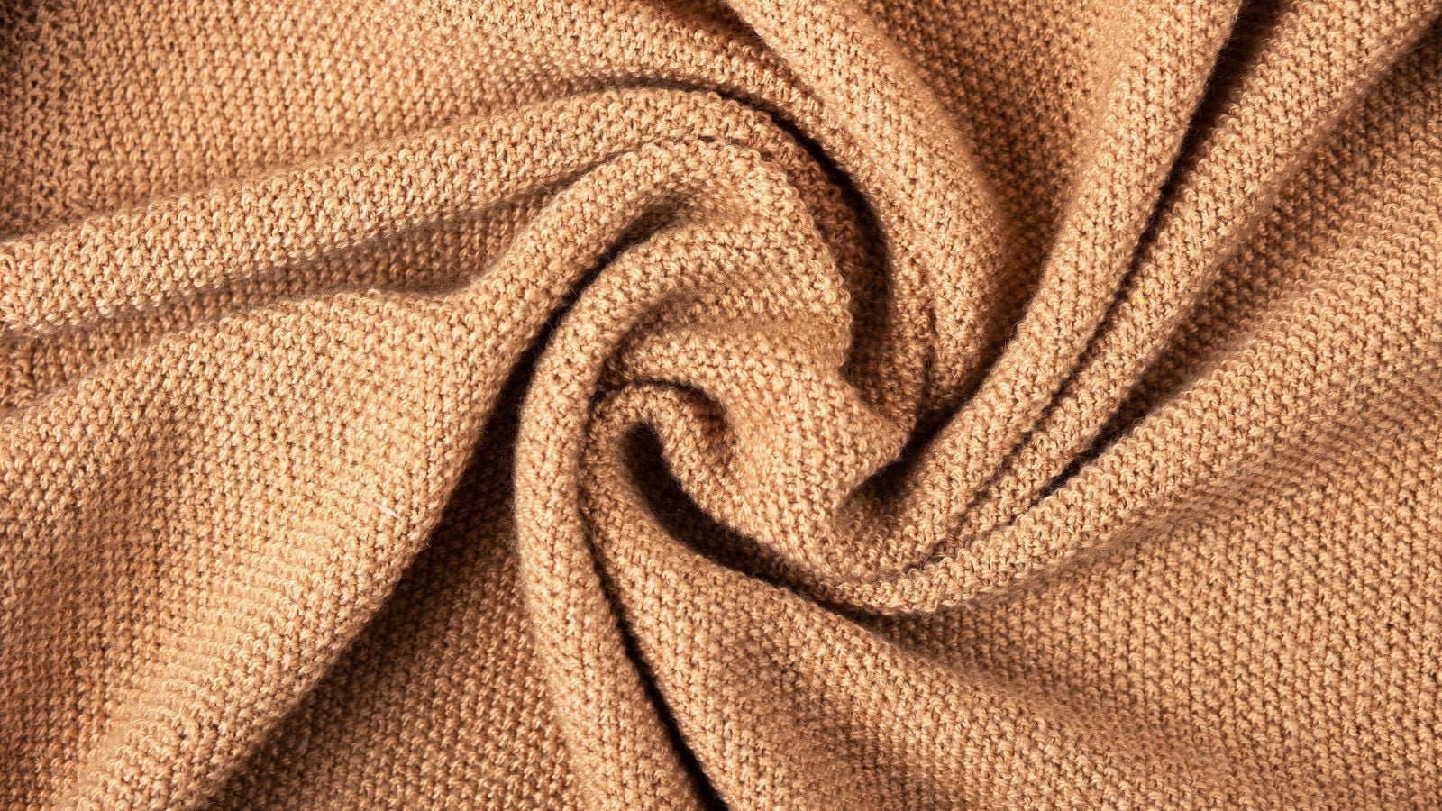 A close-up and overhead shot of a beige colored acrylic fabric, crumpled and placed on a well lit area