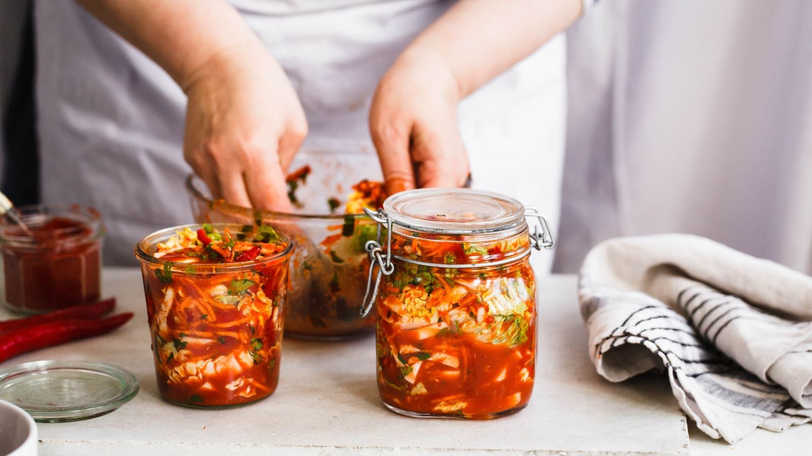 A close-up shot of a person in the process of assembling and building fermented cabbages, placing them in individual mason jars