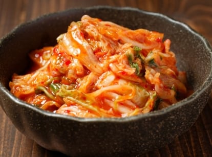 A close-up shot of a small black bowl, filled with fermented leafy greens with red, spicy paste, showcasing how long to ferment kimchi