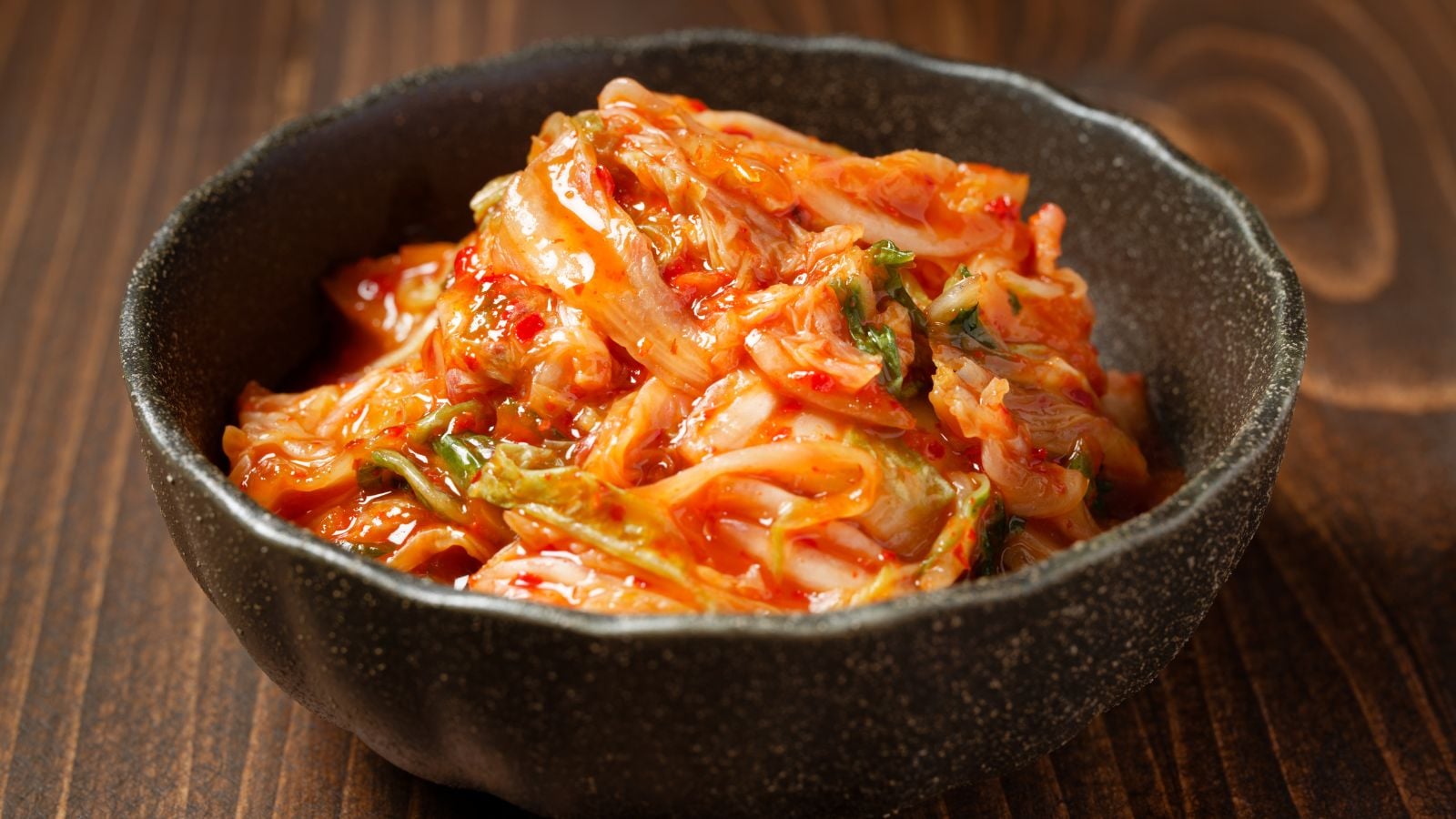 A close-up shot of a small black bowl, filled with fermented leafy greens with red, spicy paste, showcasing how long to ferment kimchi