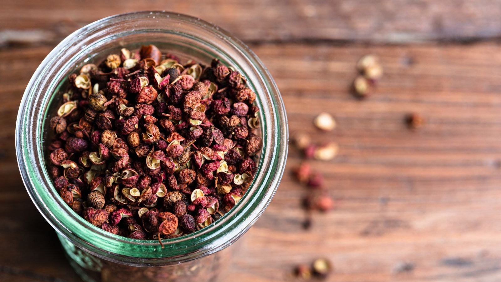 A jar full of Zanthoxylum spp. seeds harvested and dried, placed in a glass jar with some pieces scattered on the wooden surface