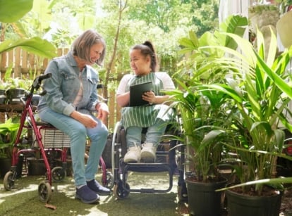 An accessible garden with two women appreciating the area, appearing to us mobility aids surrounded by lovely and lush plants with green foliage
