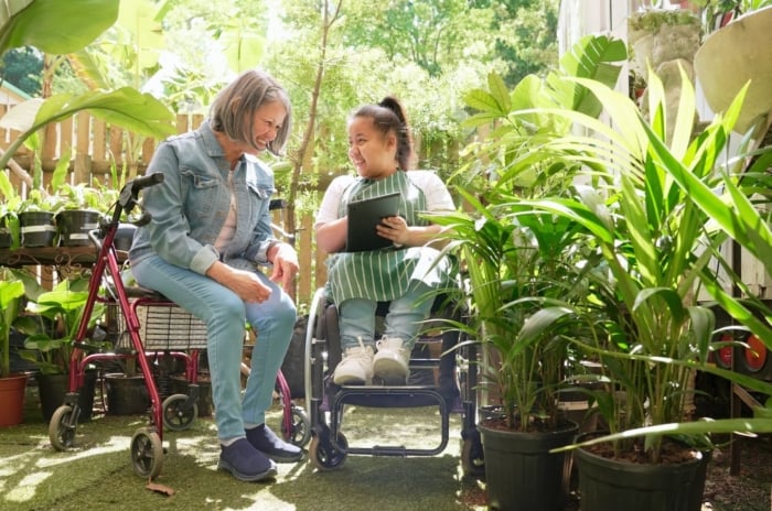 An accessible garden with two women appreciating the area, appearing to us mobility aids surrounded by lovely and lush plants with green foliage