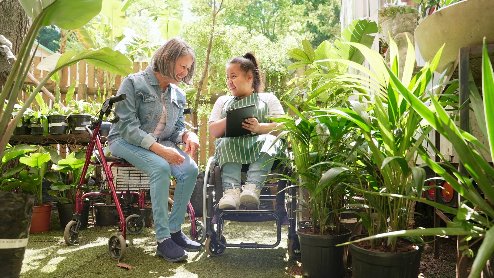 An accessible garden with two women appreciating the area, appearing to us mobility aids surrounded by lovely and lush plants with green foliage