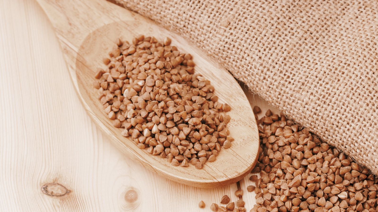Harvested Fagopyrum esculentum seeds, appearing to be placed in piles with some inside a wooden spoon while others are on a light wooden surface