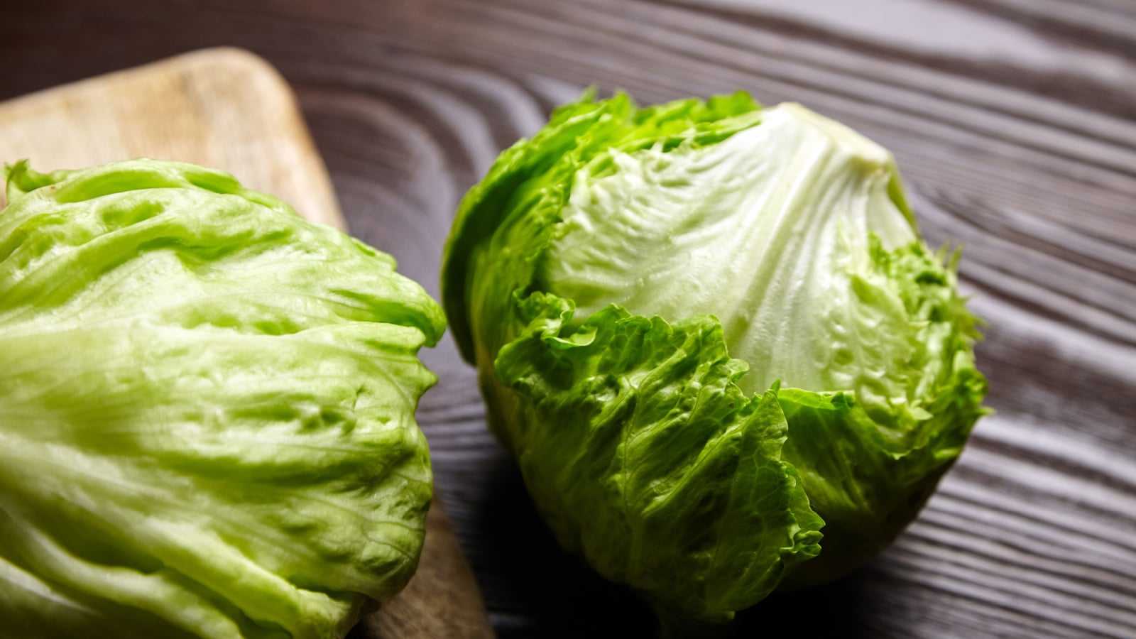 Lush, compact Lactuca sativa heads with deep green leaves on a cutting board in an indoor space on a wooden countertop.