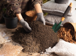 A person showing what is soil, ready to mix in various materials to enrich the mix placed on brown sheets on a table