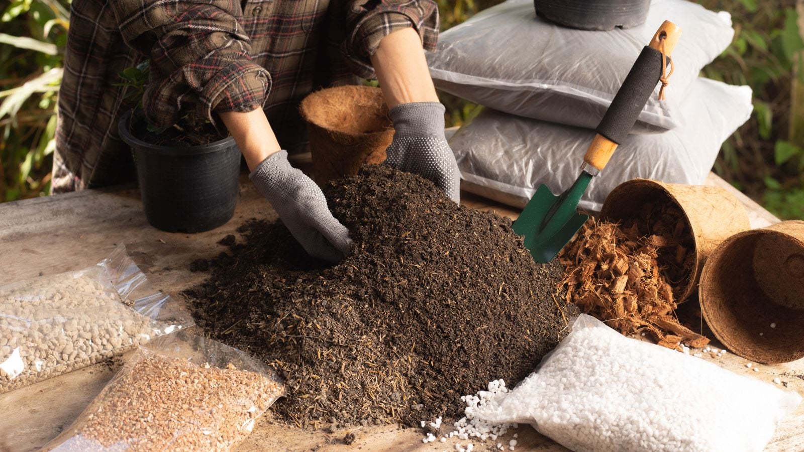 A person showing what is soil, ready to mix in various materials to enrich the mix placed on brown sheets on a table