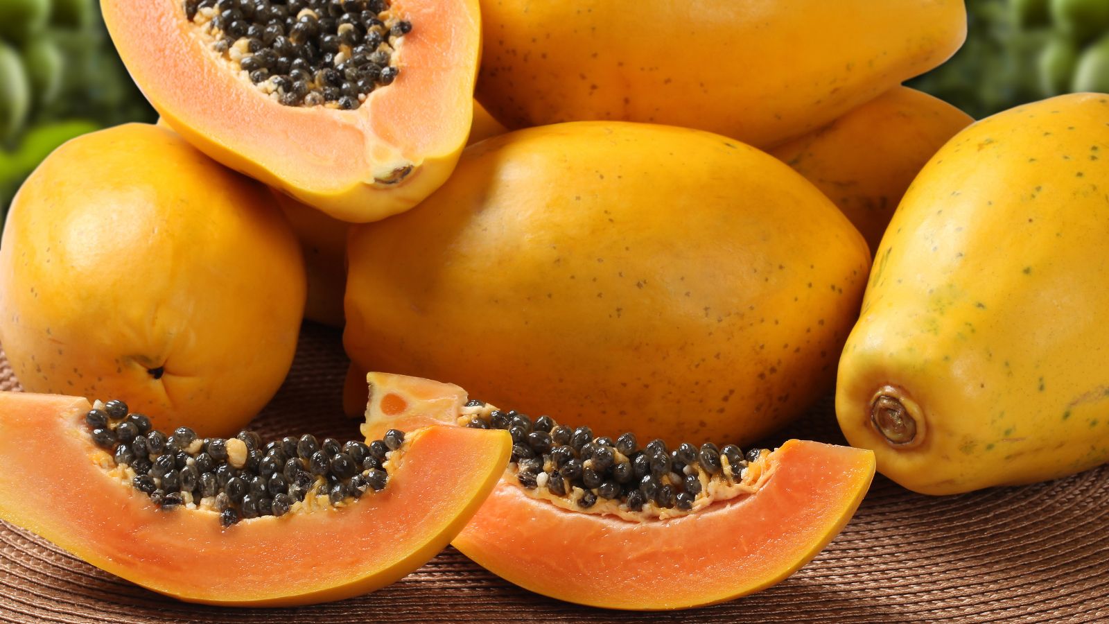 A shot of several cut and fresh ripe fruits laced on a woven mat