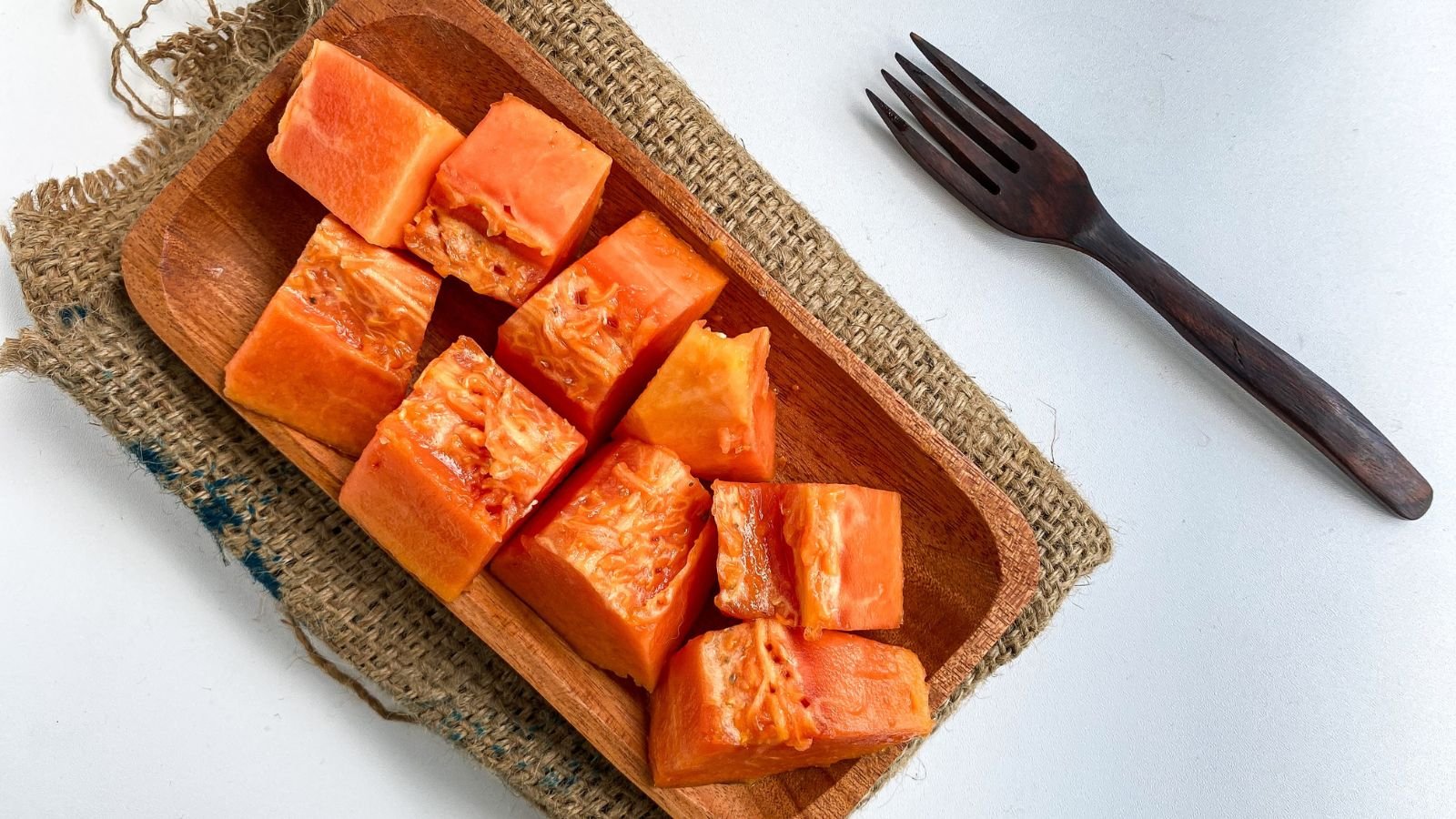 An overhead shot of cut ripe orange fruits on a wooden tray that is placed beside a fork