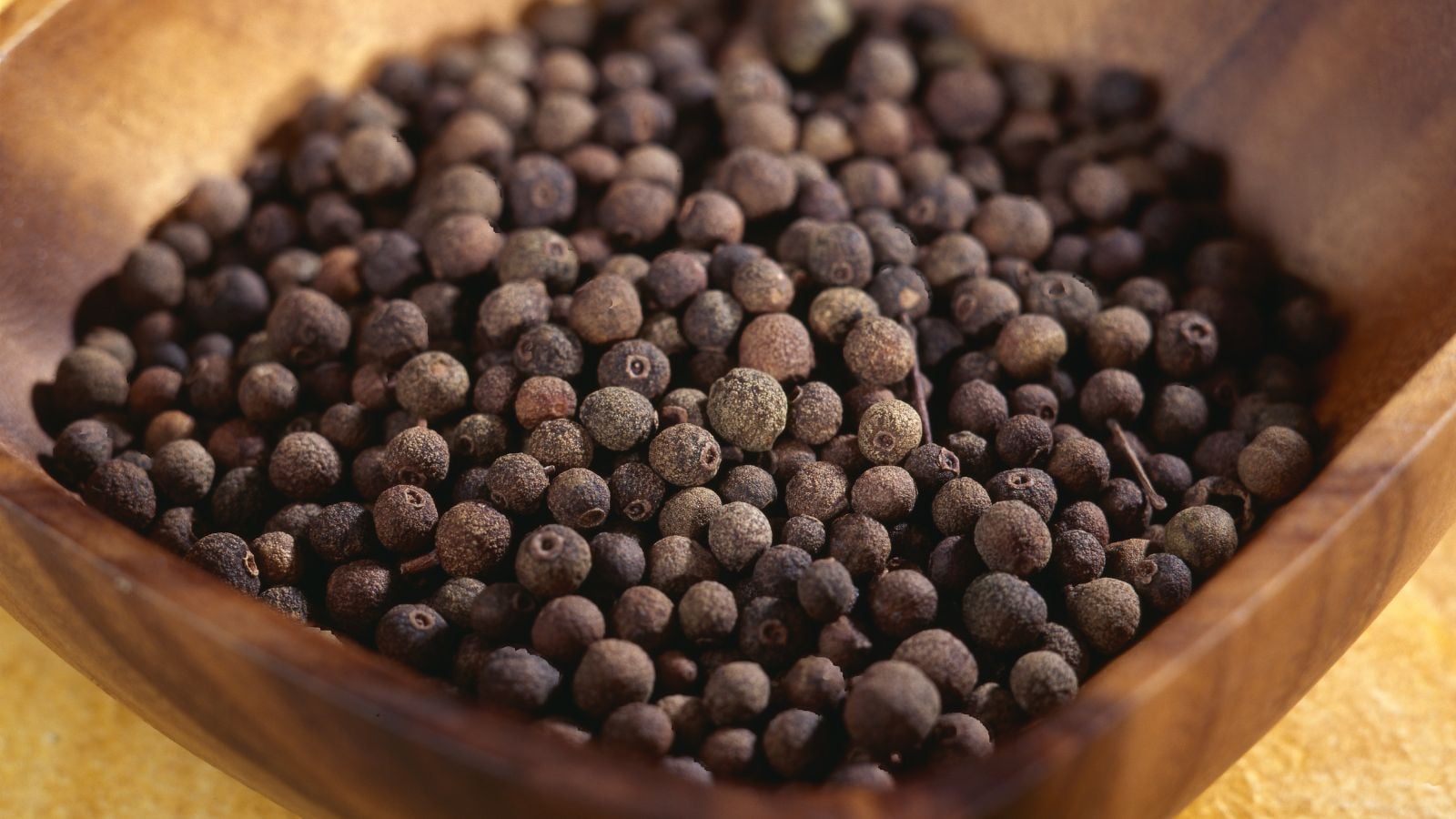 Dried Pimenta dioica berries placed inside a wooden bowl sitting somewhere with a lot of warm sunlight