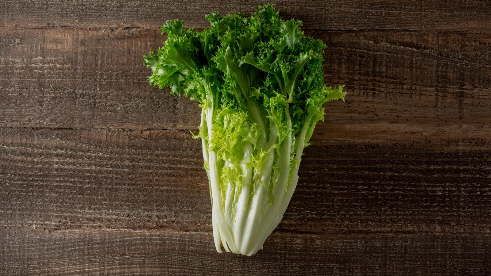 An overhead shot of a mature head of a freshly harvested leafy crop, placed on a wooden surface in a well lit area