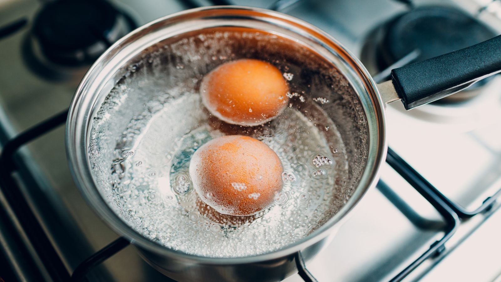 Boiling two eggs in a saucepan, with the water looking very hot appearing to bubble cooking the eggs