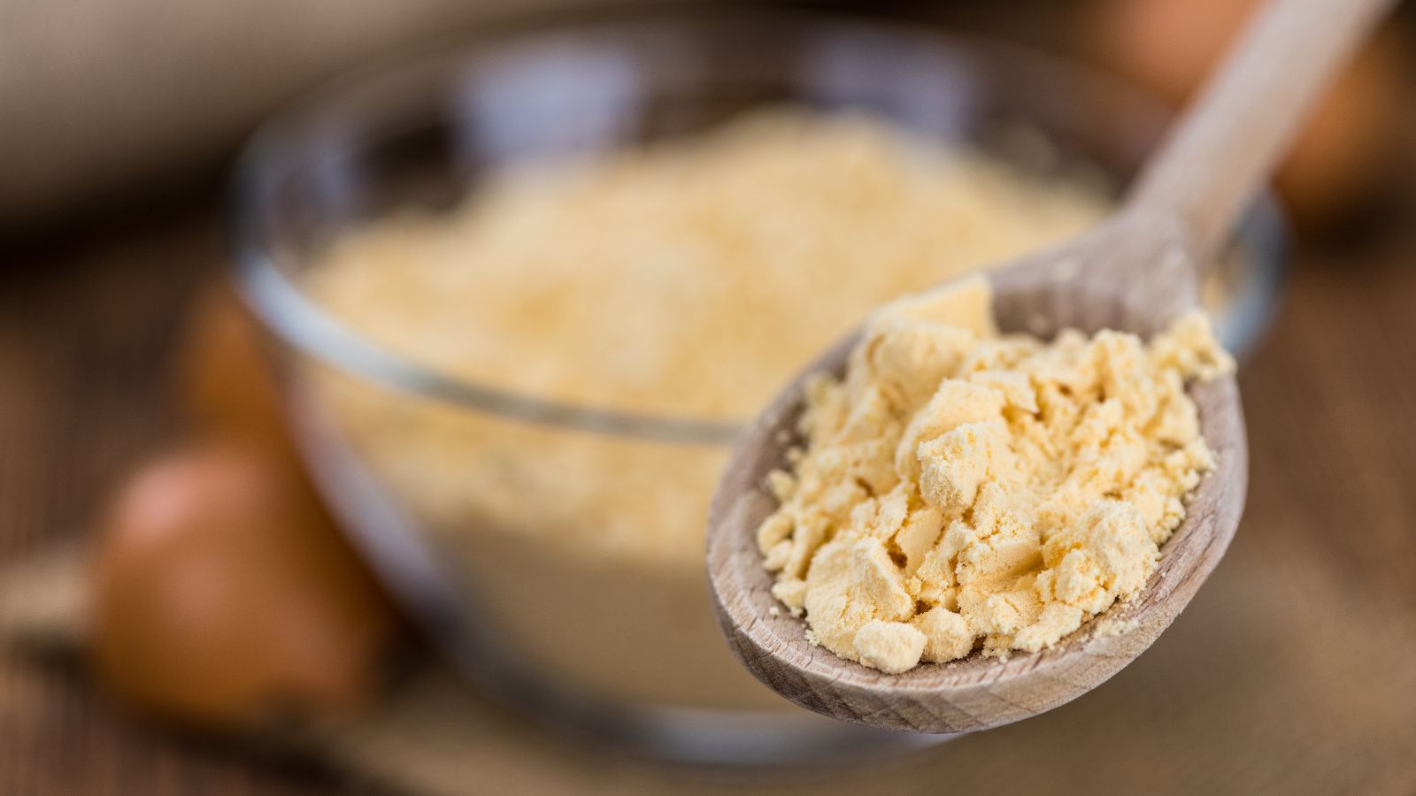 A wooden spoon filled with pale yellow powder, which is a result of dehydrating eggs