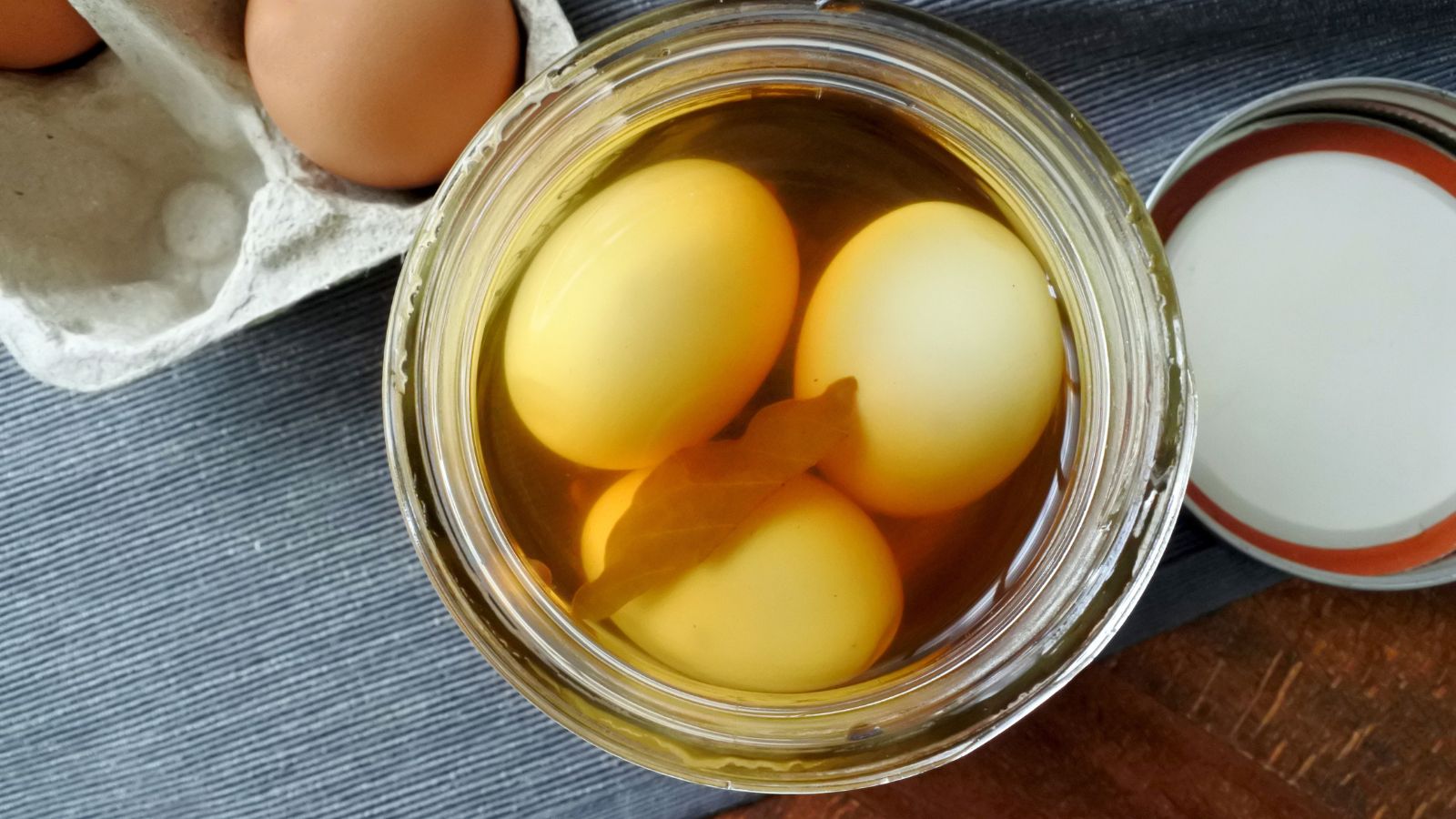Preserved eggs in a jar with water discolored, the water looking brown with some debris floating in it