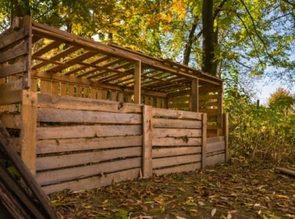 A lovely wooden DIY compost bin appearing to be placed somewhere with lots of dry leaves falling from many trees shading the bins from sunlight