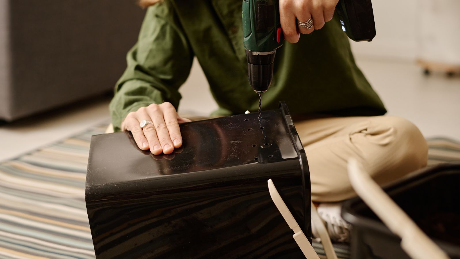 A person sitting on the floor using a tool to drill a hole into a plastic bucket